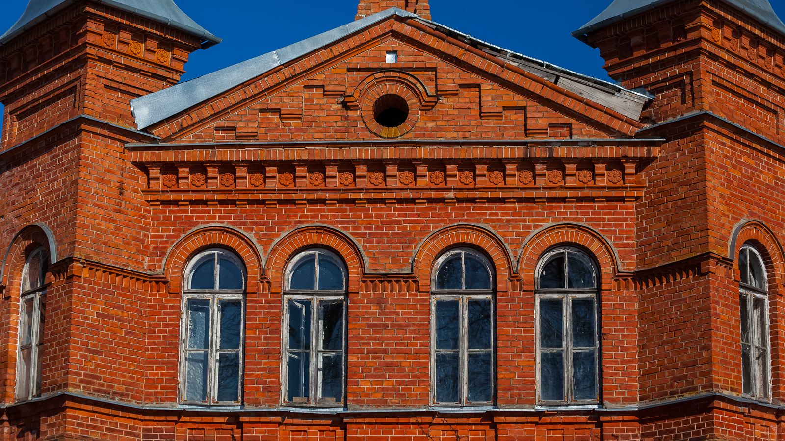 Fachada de ladrillo visto de un edificio histórico, con ventanas de arco y carpintería de madera original